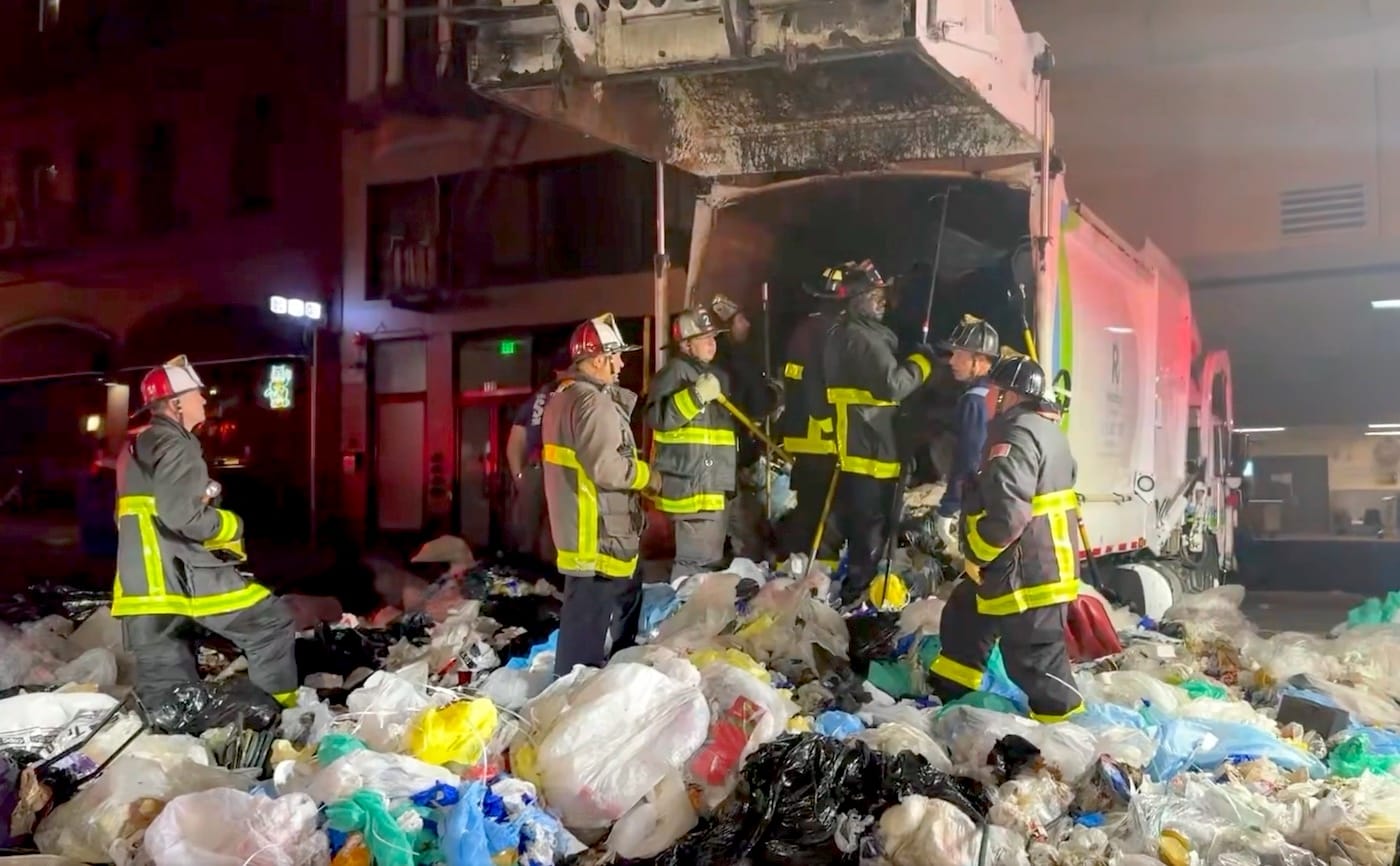 A group of firefighters in front of a Recology truck, surrounded by a large pile of trash.
